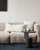 A modern living room with two cushions on the couch, both with the same pattern. One is a long lumbar and one is square, and they are made of the same artisanal handwoven cotton with a linear pattern in navy blue against soft cream. 