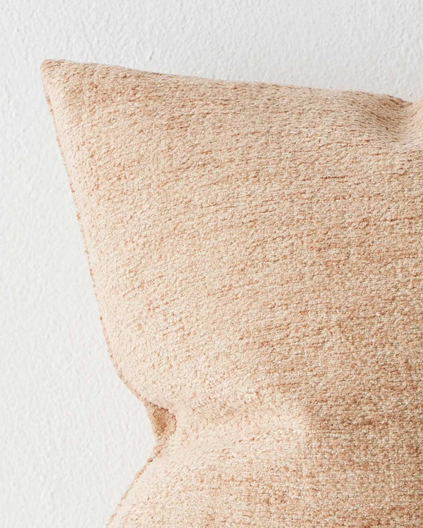The corner of a textured cushion in soft clay tones. 