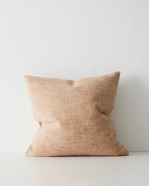 A softly textured cushion in warm light brown muted clay pink tones. 