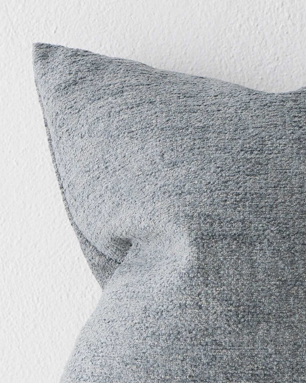 A close up image of a muted blue cushion with a soft textural element within the weave. 