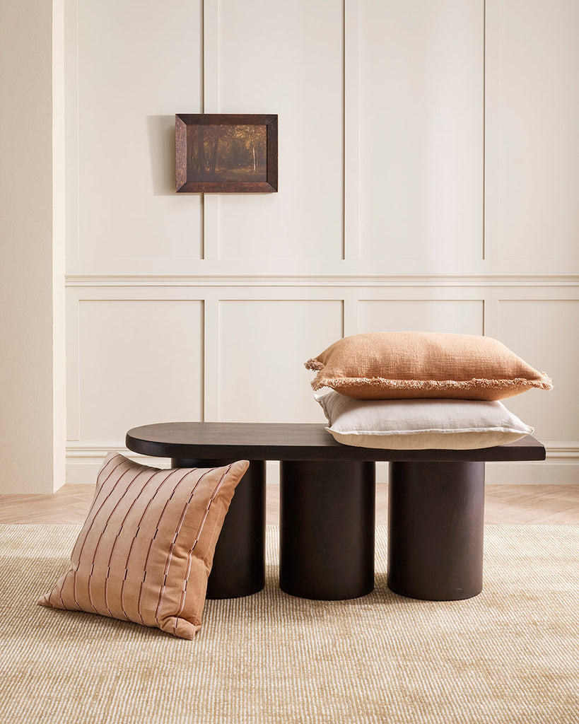 Three cushions on and around a coffee table, two in a stylish textural linen and one striped velvet in a muted clay pink. 