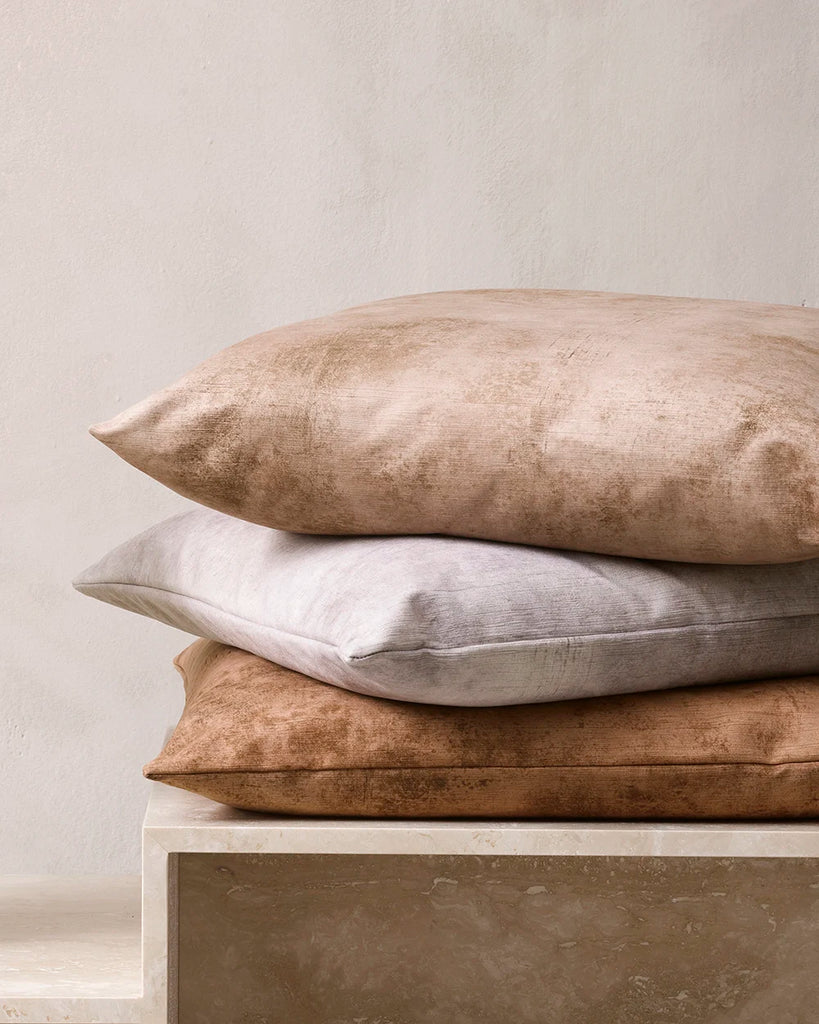 Pile of Baya Theo velvet cushions in warm brown tones