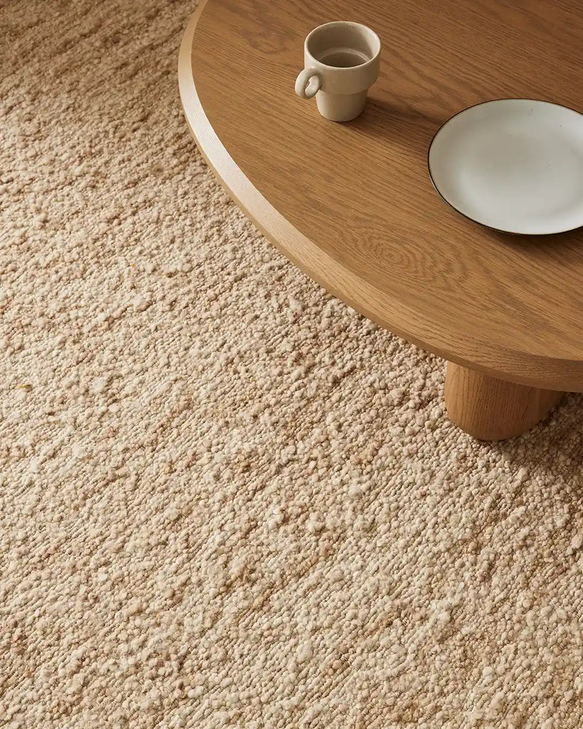 Close up view of the Henley floor rug in colour 'Ivory' showing its boucle texture and a table prop
