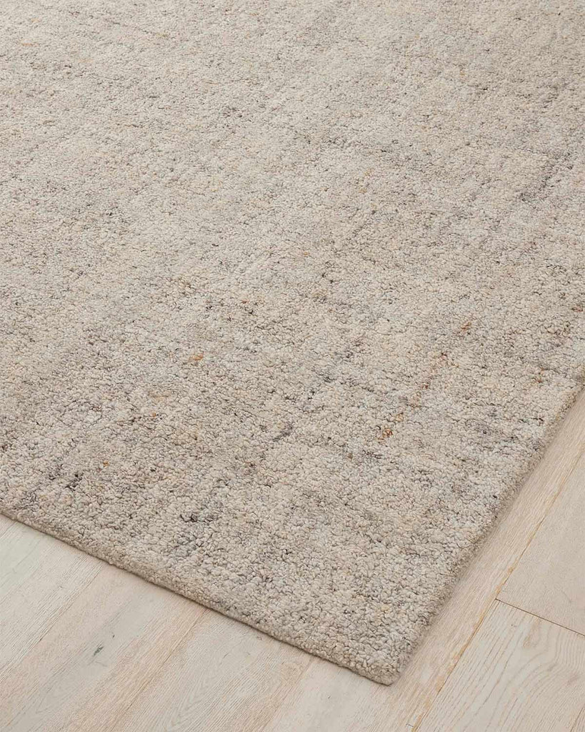 A cool beige toned textural floor rug with a very subtle pattern in darker tones, with loop piling. 