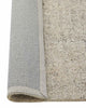 A corner image of a loop pile floor rug in off-white with the edge flipped to show the durable cotton backing. 