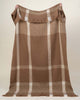 A full image of a checked throw blanket in neutral shades of nougat and brown, held up to show off it's generous sizing. 