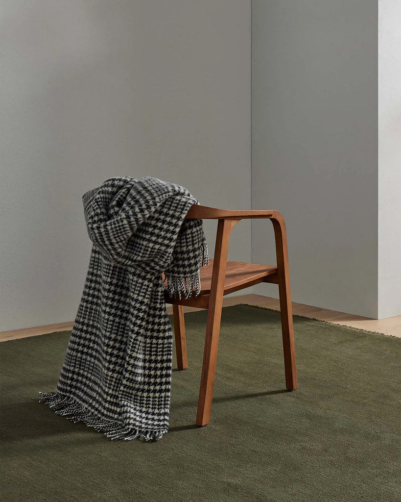 A houndstooth throw blanket in sophisticated black and white with fringed edging and 100% wool, draped over the back of a chair. 