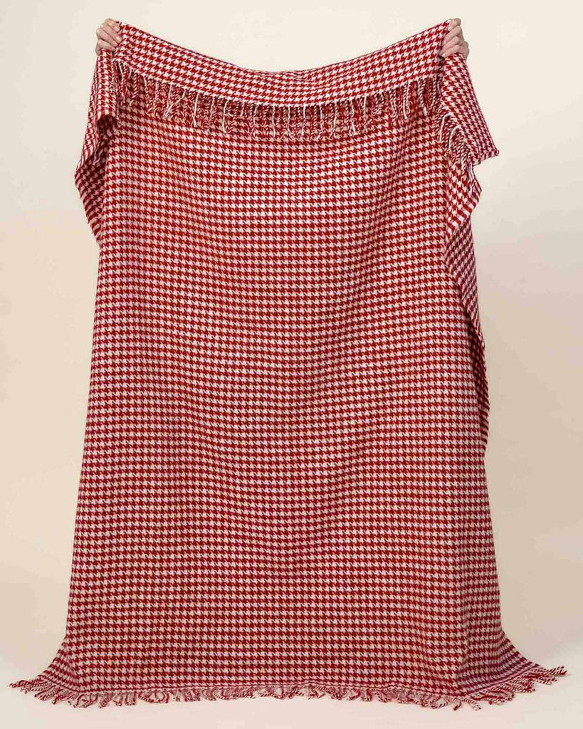 A full image of the Huxter houndstooth throw blanket in Rouge, made with 100% wool and held up to see the full generous size. 