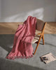 A houndstooth patterned 100% wool throw blanket in cheerful red and cream tones, draped over a wooden chair. 