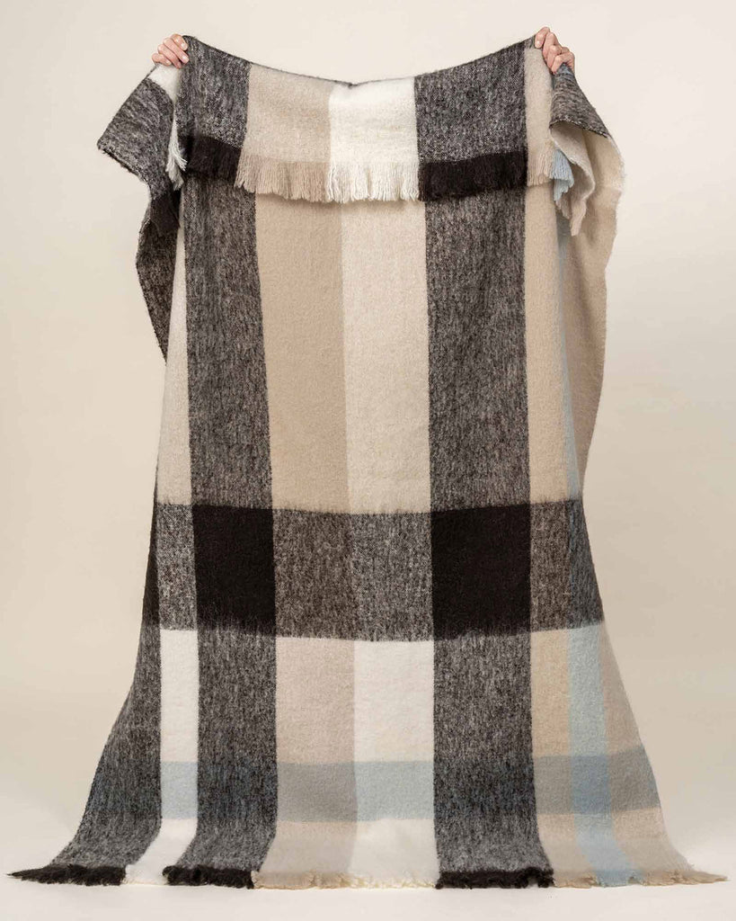 A full image of the Kinloch throw blanket in wool blend with a checked pattern in neutral tones of beige, taupe, brown and blue. 