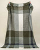 A large throw blanket in olive green and cream check, in a wool blend with fringed edges. 