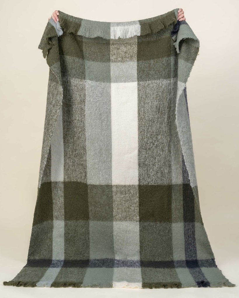 A large throw blanket in olive green and cream check, in a wool blend with fringed edges. 