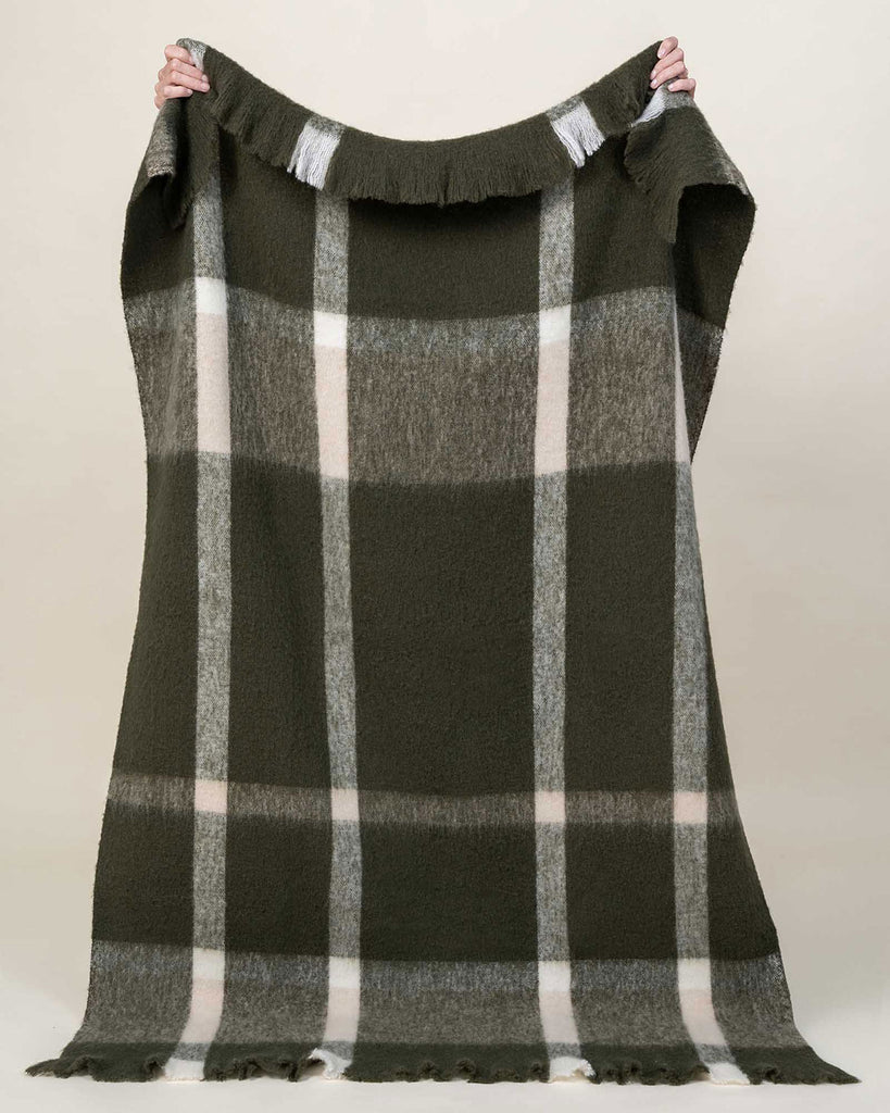 A full image of the Mayfield wool blend throw blanket, showing off the sophisticated cosy check pattern in deep green and creamy white. 