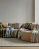 A couch with a multitude of Weave Home's new season of throw blankets, in soft earth tones. 