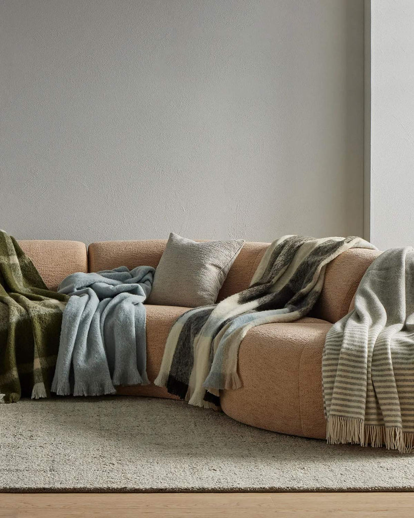 A couch with a multitude of Weave Home's new season of throw blankets, in soft earth tones. 