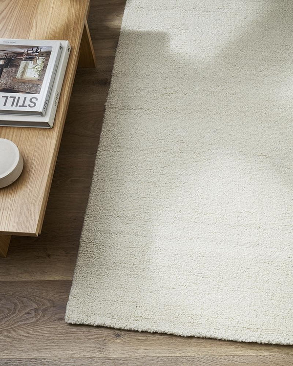 A light creamy white wool floor rug with a boucle style weave, seen on a modern living room floor - the Dorset natural White by Baya