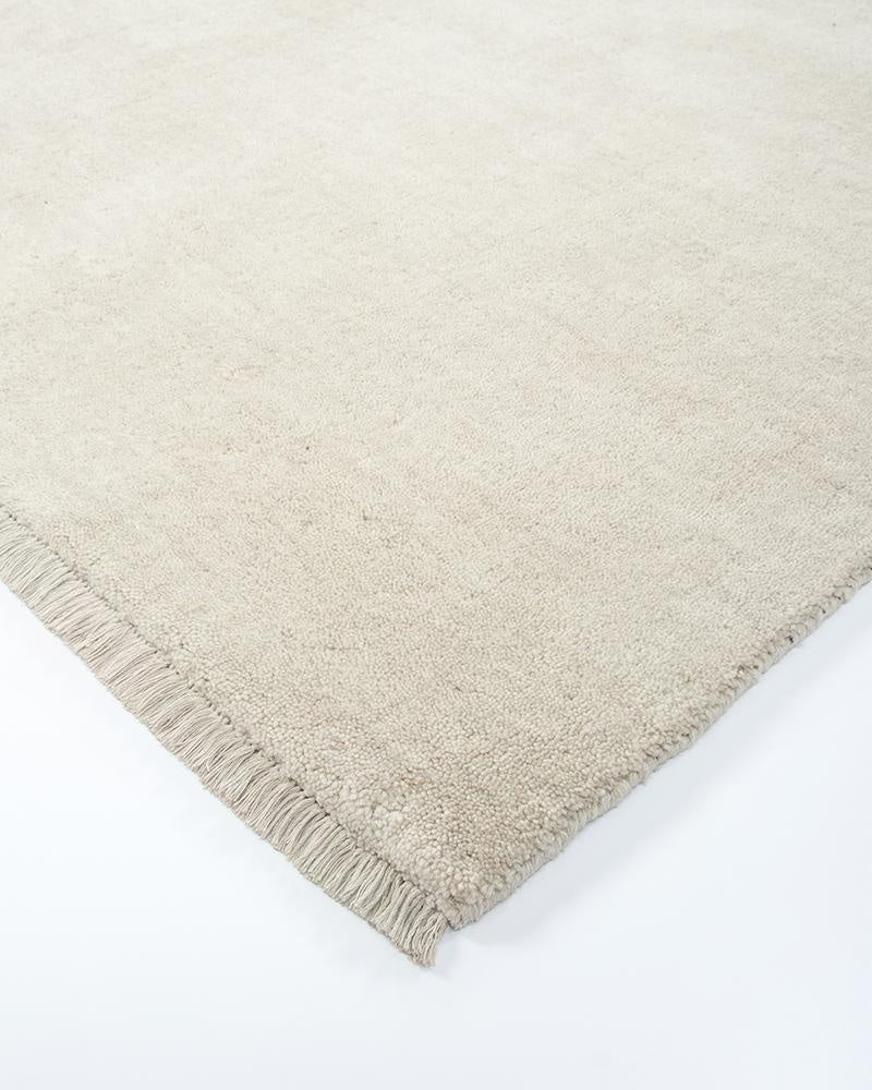 The Sandringham  creamy white 'merino' 100% wool floor rug with fringe detail, seen close up at a corner showing the fringe detail and wool cut pile.