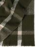 A folded throw blanket in shades of deep olive green and cream, with a fringed edging. 