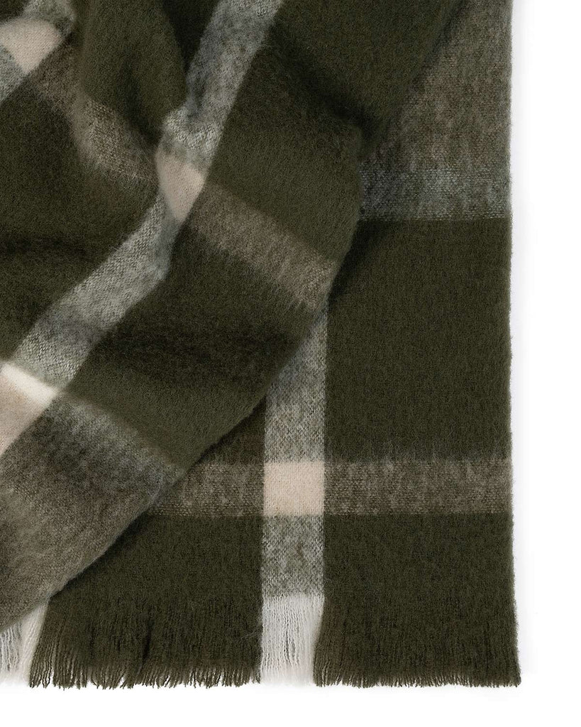 A folded throw blanket in shades of deep olive green and cream, with a fringed edging. 
