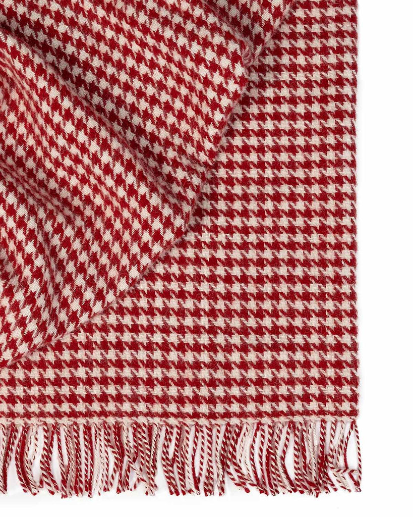A folded throw blanket with a houndstooth pattern in red and white and with a twisted fringe edge. 