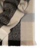 A folded throw blanket in shades of warm beige, chocolate brown and sky blue, with fringed edges. 
