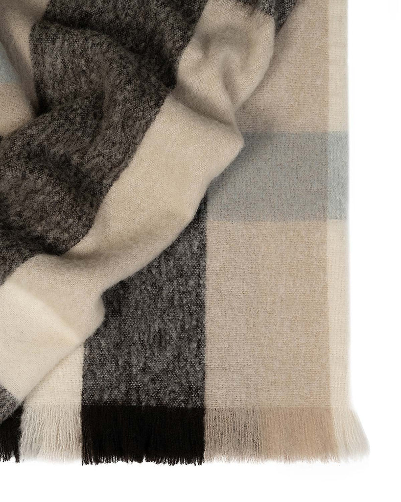 A folded throw blanket in shades of warm beige, chocolate brown and sky blue, with fringed edges. 