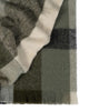 A folded throw blanket in an on trend green check pattern with cream accents and fringed edges. 