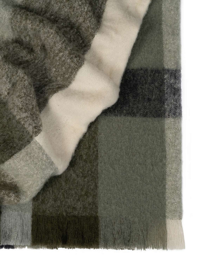 A folded throw blanket in an on trend green check pattern with cream accents and fringed edges. 