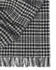 A folded throw blanket in 100% wool with a sophisticated black and white houndstooth check pattern and twisted fringe edging.