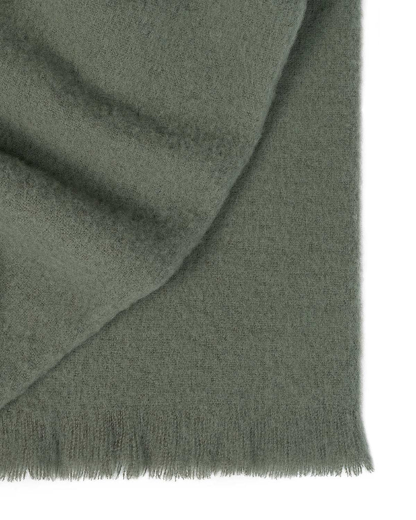 A folded soft wool blend throw blanket, with fringed edges, in a delicate shade of muted green. 