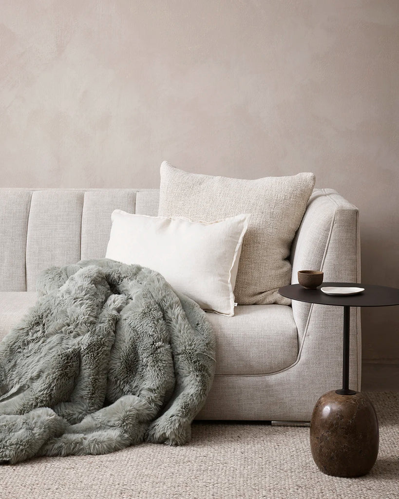 Baya green 'Seafoam' faux fur throw blanket draped over a sofa in a contemporary living room