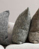 Three cushions with textural weaves, in earth toned shades of green, brown, and slate, styled on a couch by Baya. 