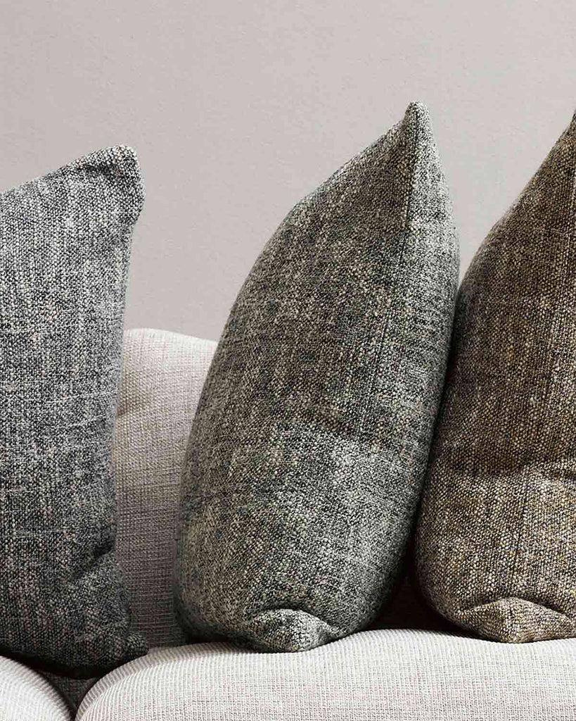 Three cushions with textural weaves, in earth toned shades of green, brown, and slate, styled on a couch by Baya. 