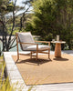 A warm brown rug by Baya NZ in the shade Teak, depicted outside on a sunny day with a chair and table. 