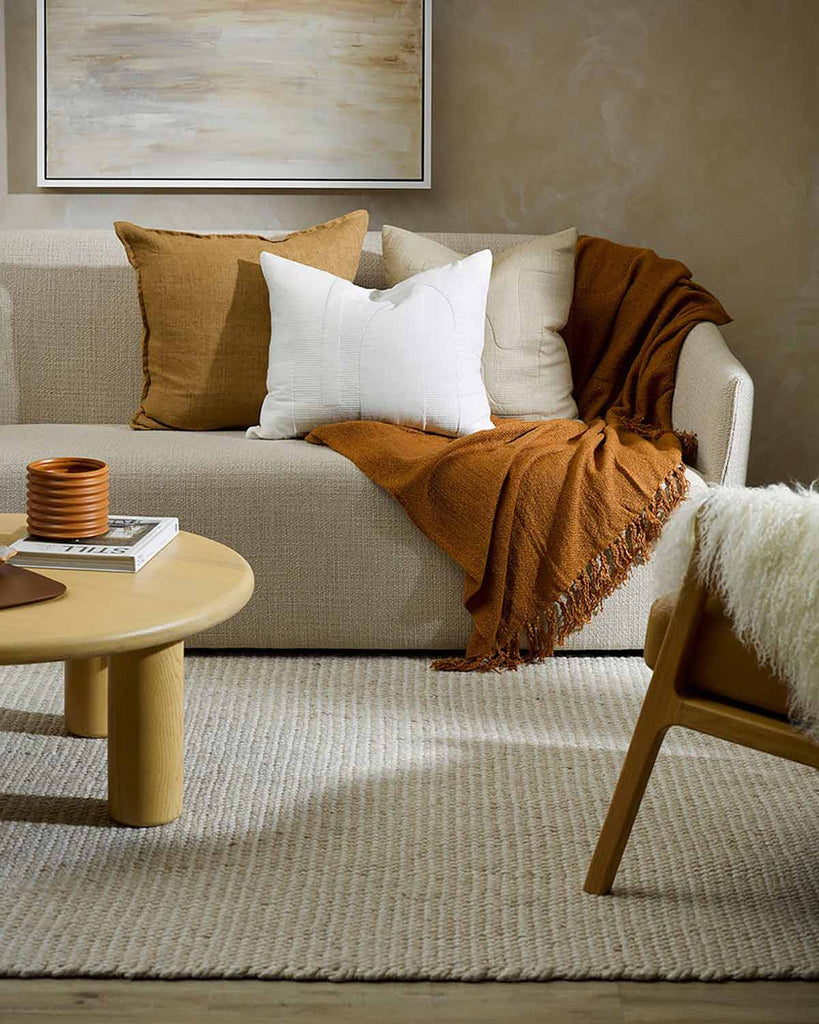 A cozy looking couch styled with pillows and throws in a modern living room, with a rug by Baya NZ