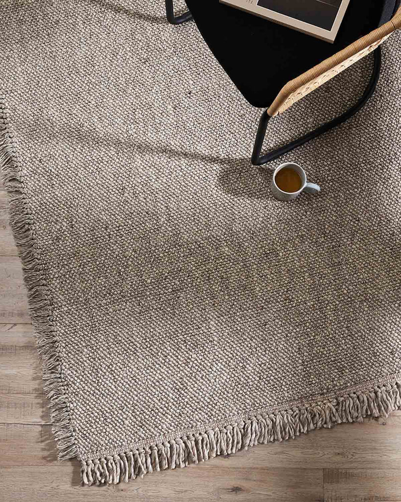 A top view of a neutral taupe rug by Baya NZ with a chair and a cup of coffee.