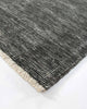 A corner image of the Corbett floor rug, in shade Peat, a soft charcoal with contemporary distressing with a short cream fringe. By Baya