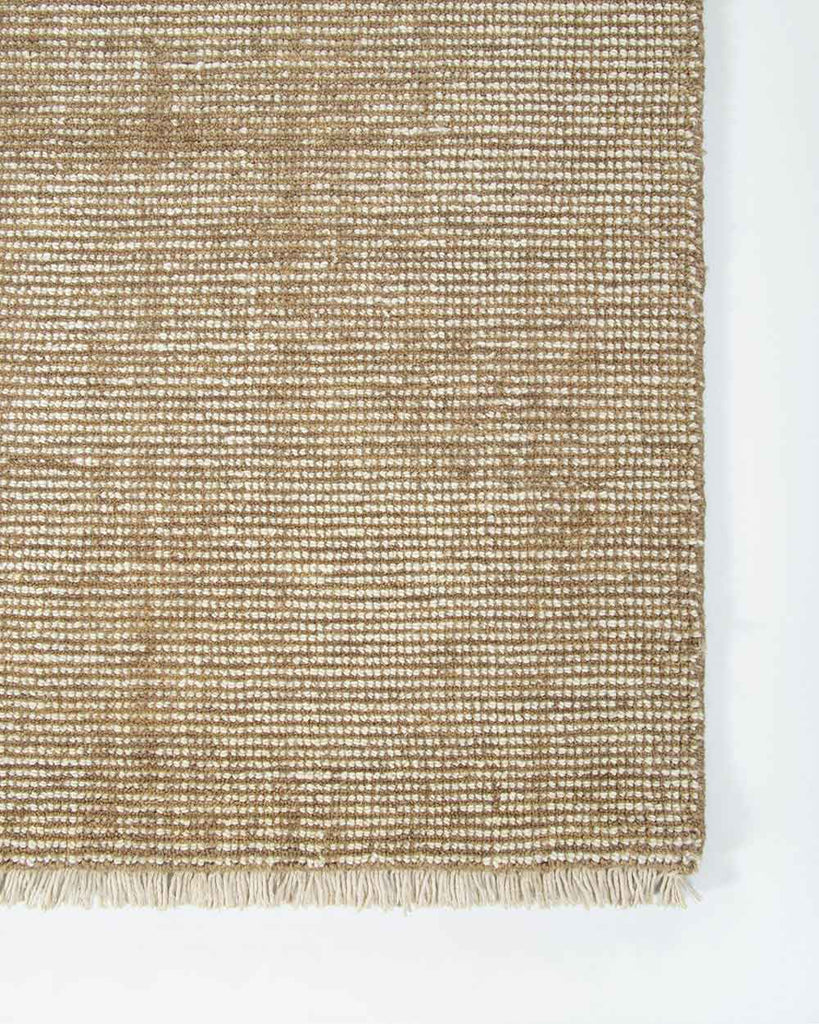 A corner image from above of the Corbett floor rug in the shade Honey, a lightly distressed contemporary warm beige, with cream detailing and a short creamy fringe. By Baya
