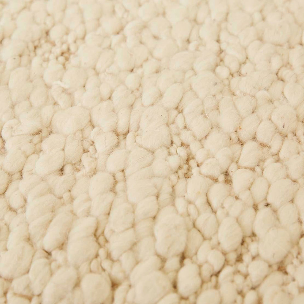 Close up of the weave of a textural wool blend boucle style rug by Globe West and Soren Liv NZ in shades of warm ivory and cream. 