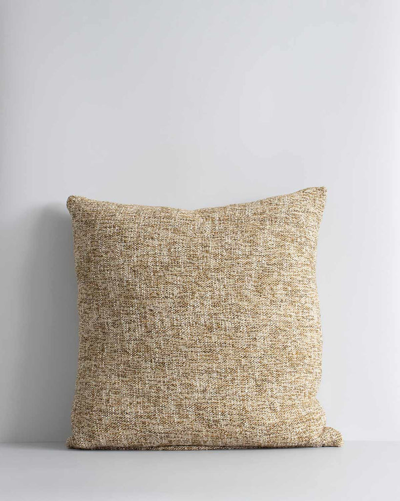 A textural woven cushion in shades of muted mustard yellow and ercu, by Baya