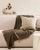 A textural woven cushion in shades of creamy oat and ercu, styled in a modern living room with shades of cream and brown, by Baya