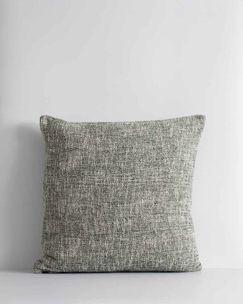 A textural cushion in shades of sage green and ercu, with a prominent weave, by Baya. 