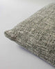 Corner view of a textural cushion in shades of sage green and ercu, with a prominent weave, by Baya. 