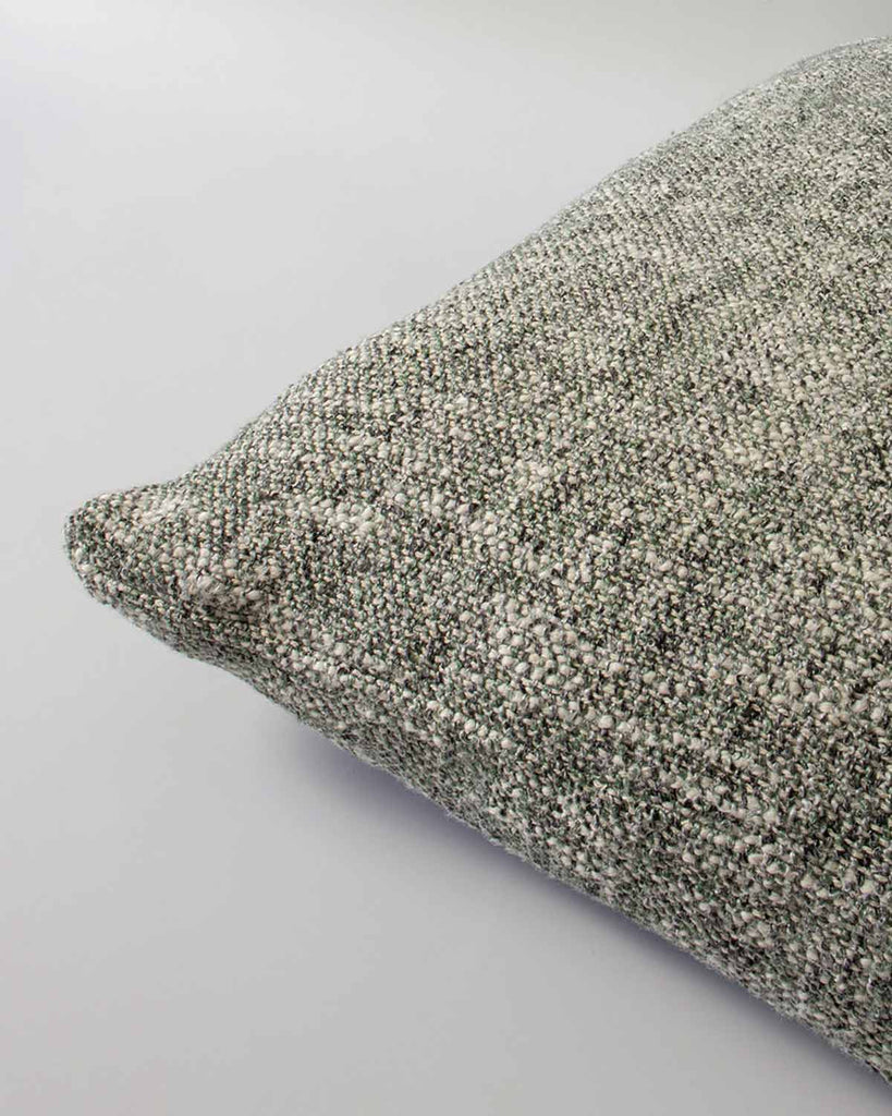 Corner view of a textural cushion in shades of sage green and ercu, with a prominent weave, by Baya. 
