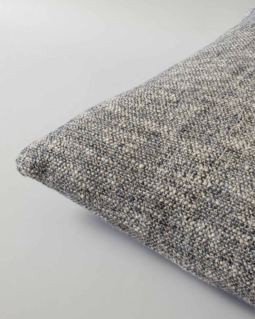 Corner view of a textural woven cushion in shades of slate, blue-black and ercu, by Baya
