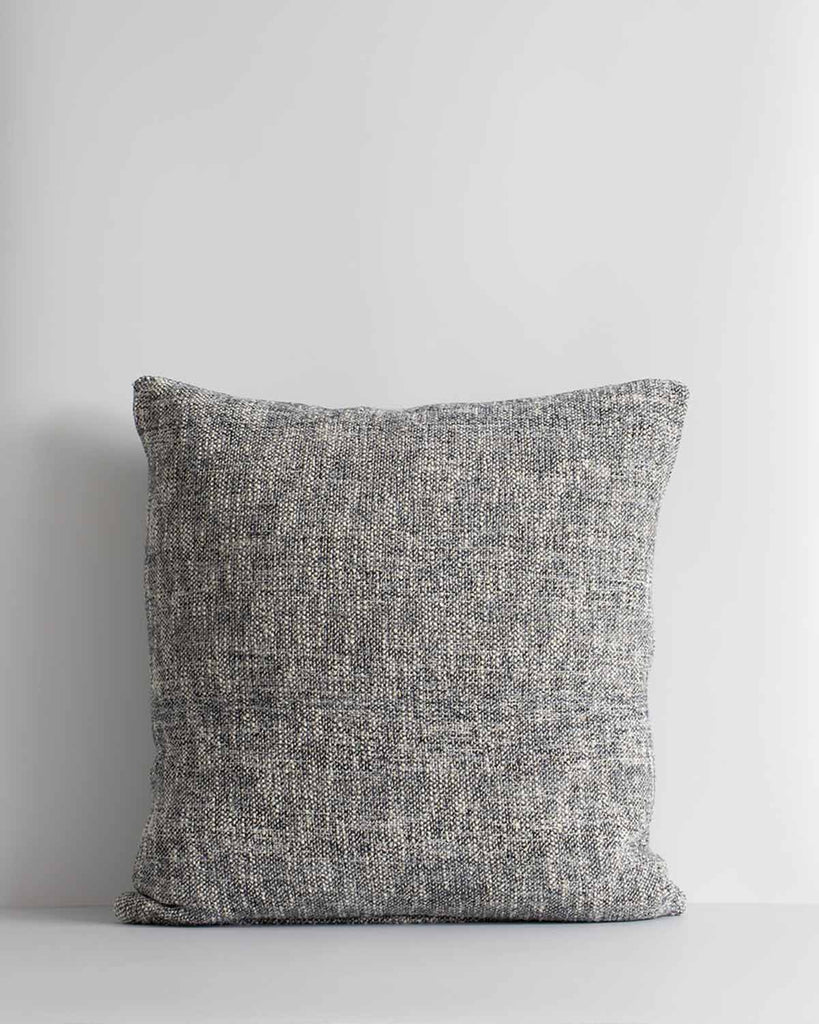 A textural woven cushion in shades of slate, blue-black and ercu, by Baya