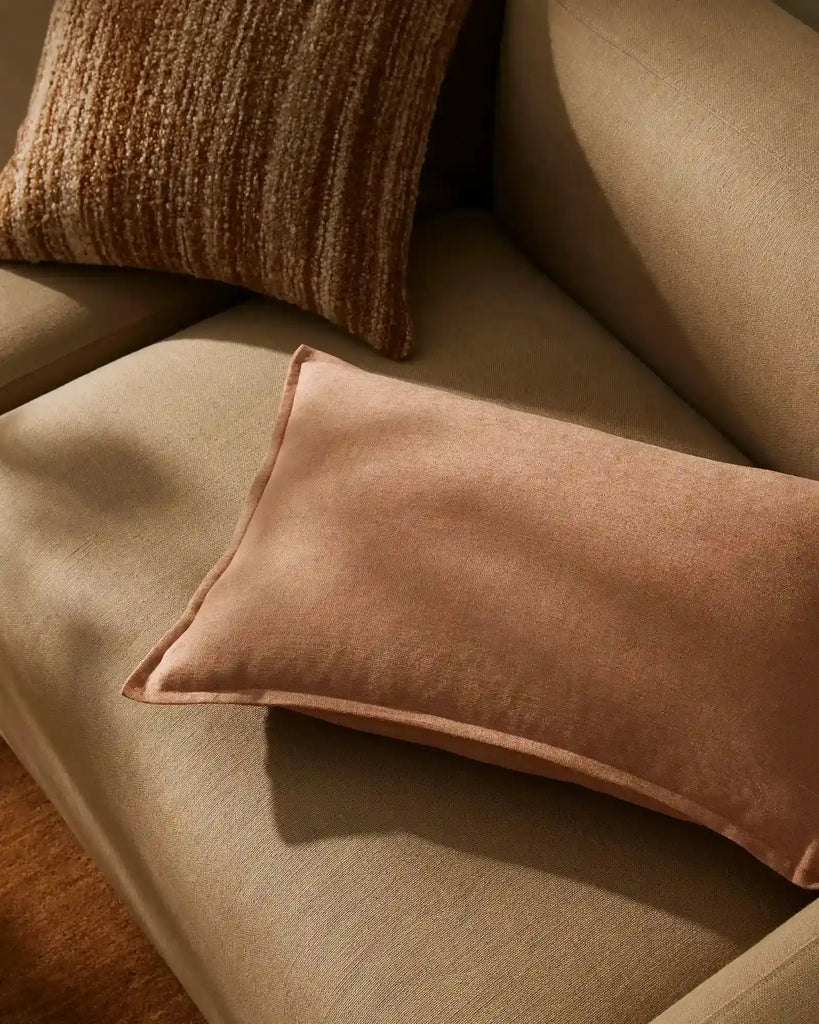 A soft pink clay colouored cushion with a vintage vibe, seen on a cpale brown couch