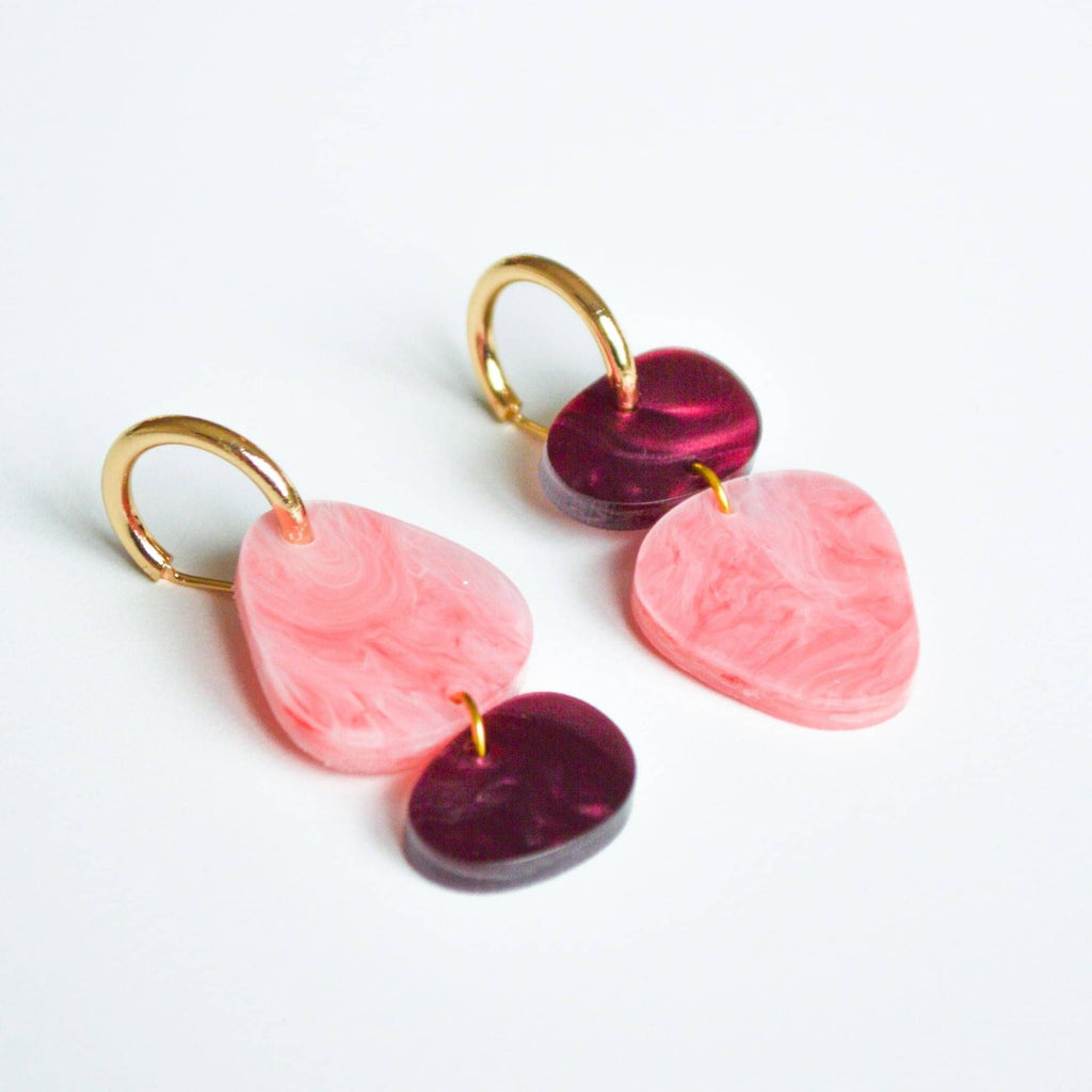 A pair of acrylic earrings in organic shapes with charms in coral pink and merlot shades. 