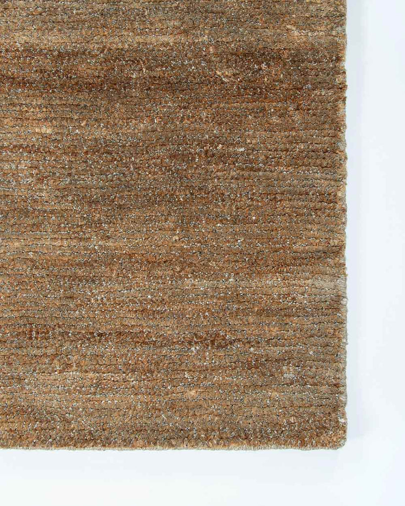 A corner image of the Fairbanks floor rug in shade Sand, a deliciously warm toned brown handwoven piece. 
