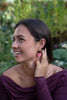 A woman wearing a gold hoop earring with two organic shaped charms in deep merlot red and marbled coral pink.